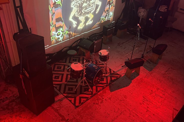 A railway arch, with a projection screen, PA system, and monitors set up. Lit by red light, with a projection saying 'Piehouse Co-Op' and a drawing of a pie man.