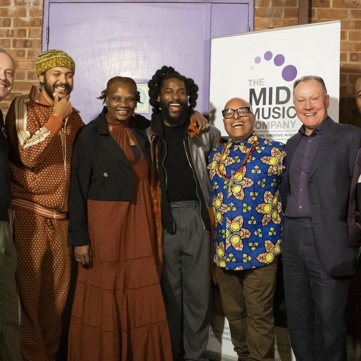 The founder, board members, and patrons of The Midi Music Company smile and laugh while posing for a photo at the 30th anniversary celebration. A banner behind them reads "The Midi Music Company."