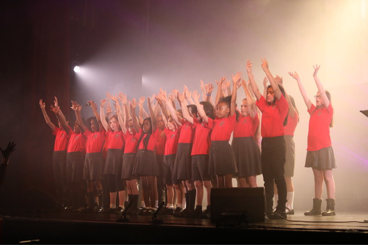 Primary school class performing on stage with hands in the air