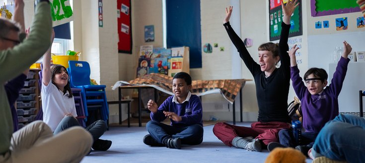 Children in on carpet in classroom arms raised