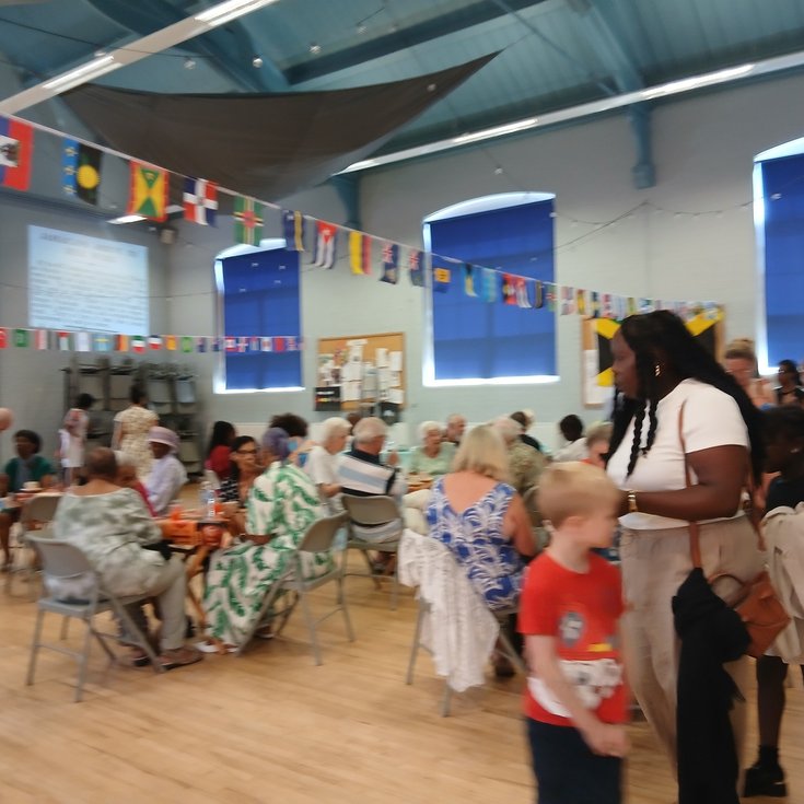 packed community hall decorated with flags. People mingle with drinks and hot food and are entertained.
