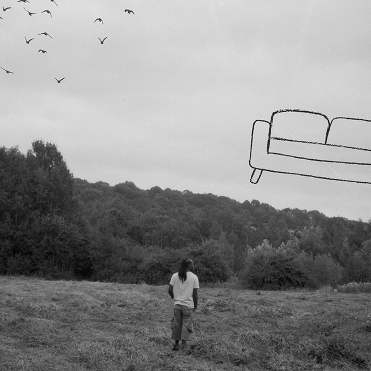Woman in a field in the distance with sofa outline drawn in the sky