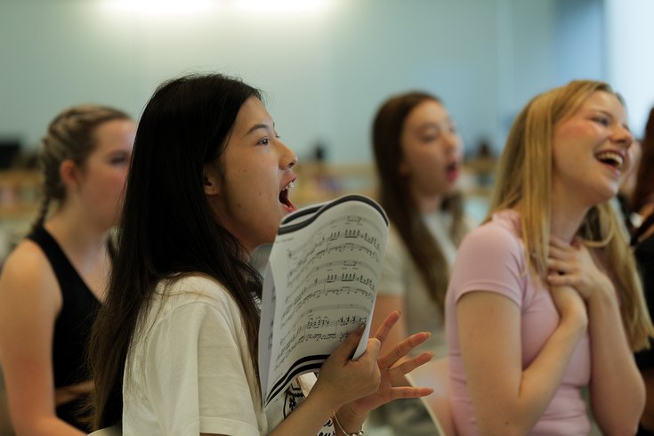 A group of Musical Theatre Summer School Participants are sat singing