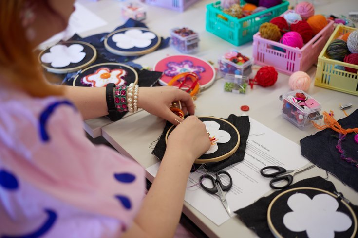 Close-up of hands working on an embroidered flower on black fabric.