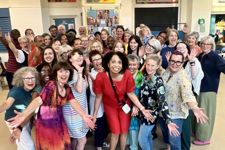 A group of grinning people in brightly coloured clothes holding arms out in welcome