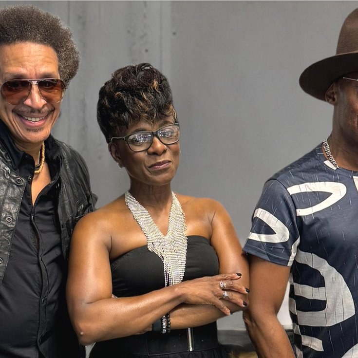 The stylish members of Loose Ends pose confidently. One in a leather jacket and sunglasses, another in a sparkling top, and the third in a patterned shirt and wide-brimmed hat.