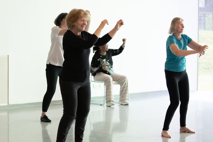 Group of over 60s participants  dancing together in a studio. One person is seated, some are standing.
