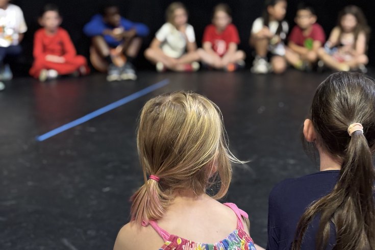The back of some students' heads as they sit in a circle on stage.