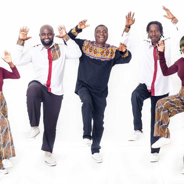 5 singers in a group with hands in the air and one leg lifted. Each singer wears an outfit of red, black and white