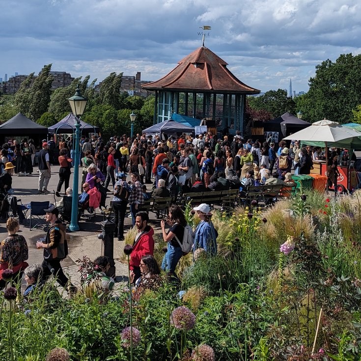 Event at the Horniman Bandstand with visitors and stalls, and London skyline in the background