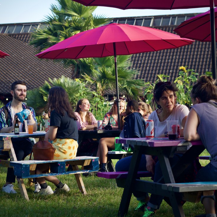 A photo of people sat on picnic benches in the Albany garden on a summer evening