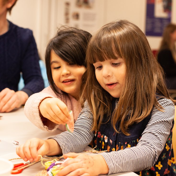 Two young girls making a rope creation at a table.