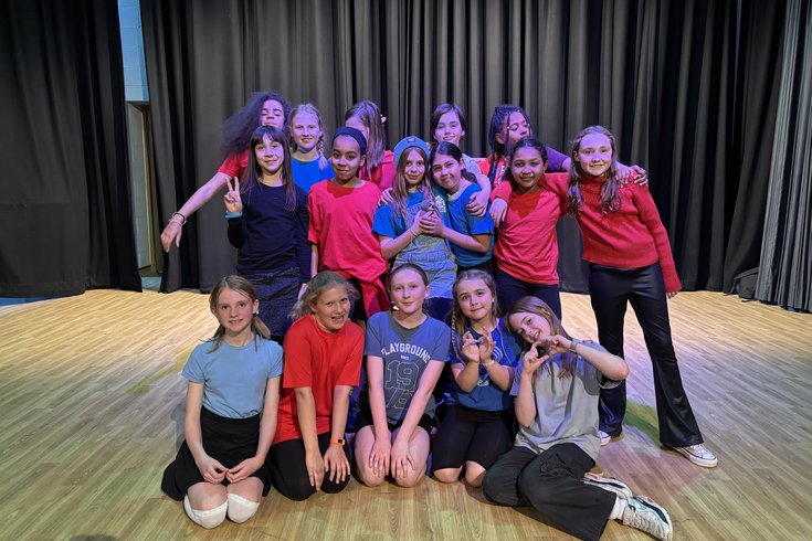 A group of students posing for a cast photo on stage in red and blue costumes.