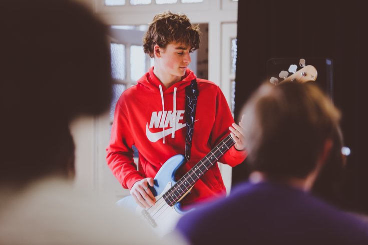 A young person in a red top plays the bass guitar.