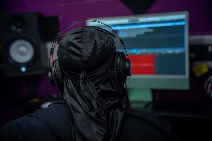 A photo of a young man from the back, wearing headphones and looking at a computer screen.