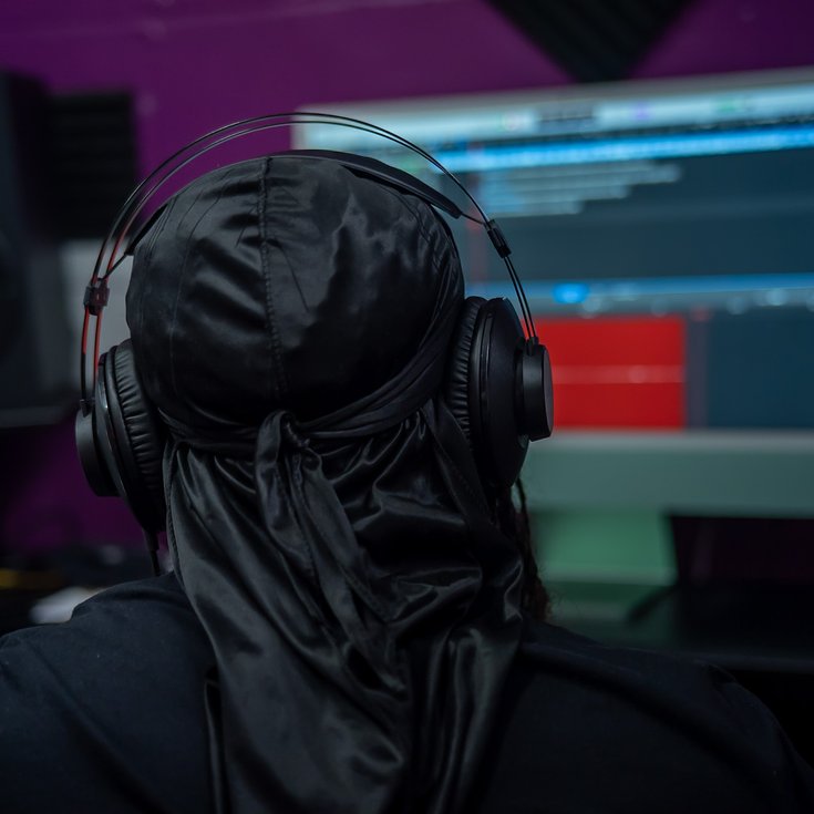 A photo of a young man from the back, wearing headphones and looking at a computer screen.