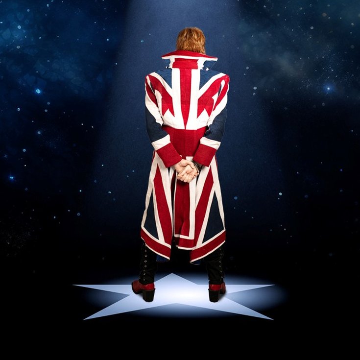 Person in a Union Jack coat stands on a star-shaped spotlight, against a starry night sky, hands clasped