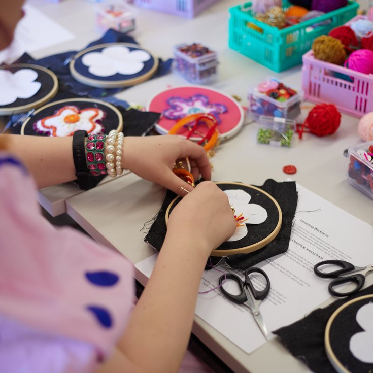 Close-up of hands working on an embroidered flower on black fabric.
