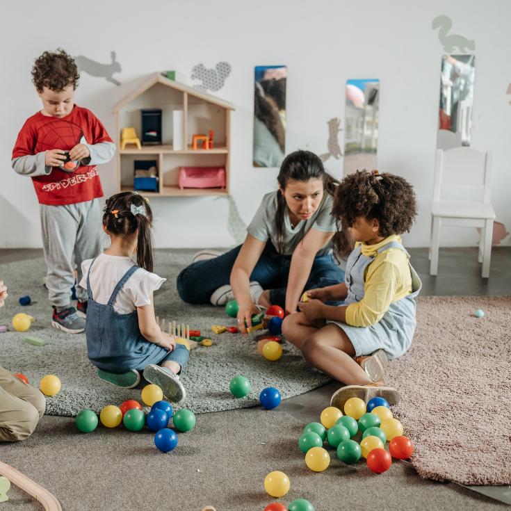 three children and nursery teacher playing in classroom