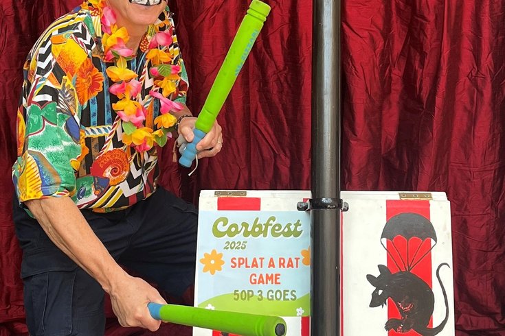 A face painted person with a brightly coloured 'Splat the Rat' game in front of a red silk curtain.