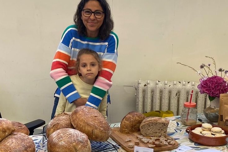 A market trader with her daughter, at her stall. The stall has sourdough bread and biscuits