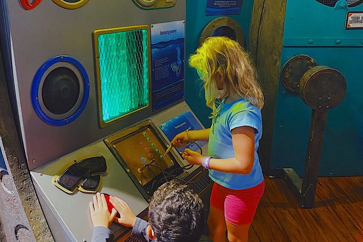 two children playing with colourful, interactive submarine-style controls