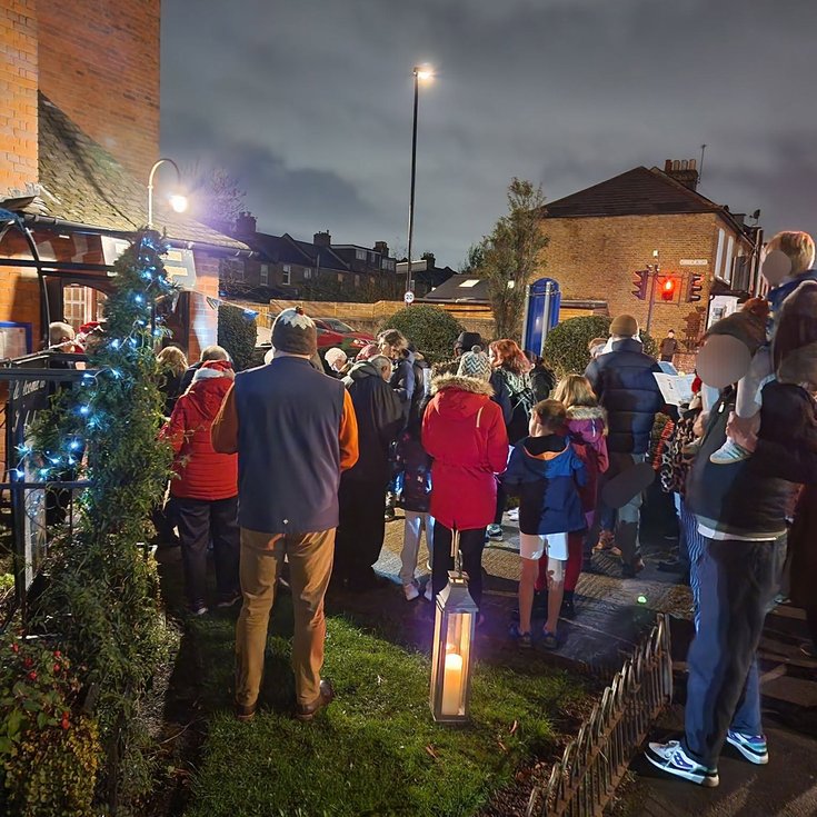 a group of people in colourful outfits gather to sing outside a church in twinkling lights