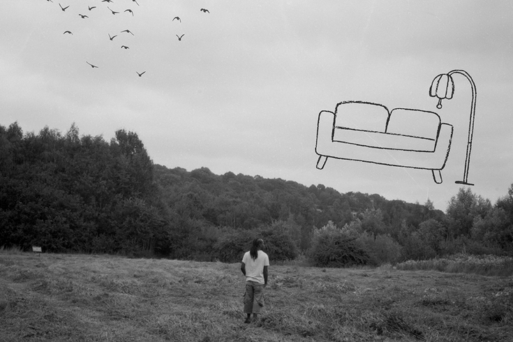 Woman in a field in the distance with sofa outline drawn in the sky