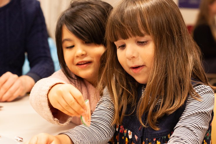 Two young girls making a rope creation at a table.
