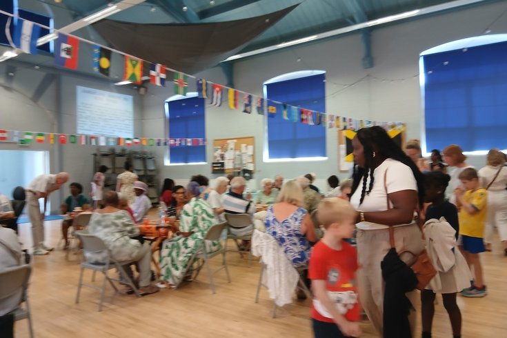 packed community hall decorated with flags. People mingle with drinks and hot food and are entertained.