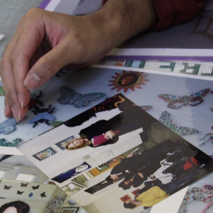 A photo of someone's hand on top of photographs showing different events, from Arts Network's archive.