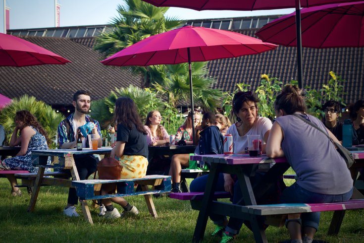 A photo of people sat on picnic benches in the Albany garden on a summer evening