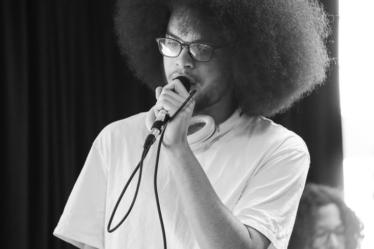 A young person with an afro raps into a mic.