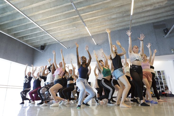 A group of Musical Theatre Summer School Participants dance in a cluster with raised hands