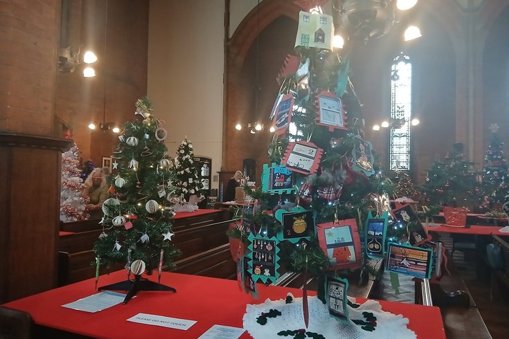 A church is decorated with many christmas trees, they have decorations on related to different interest groups.