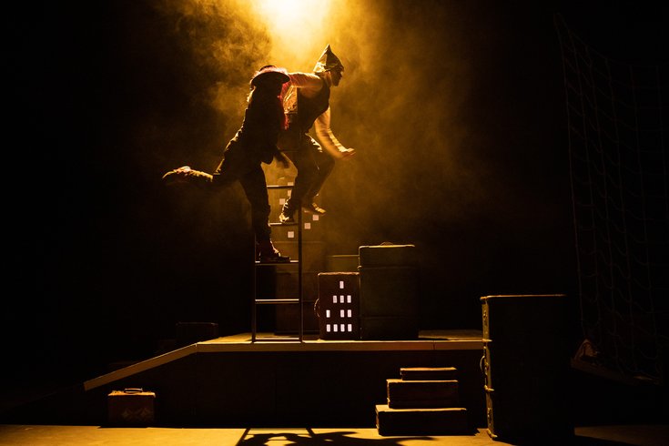 Two performers in low lighting suspended from a ladder on stage