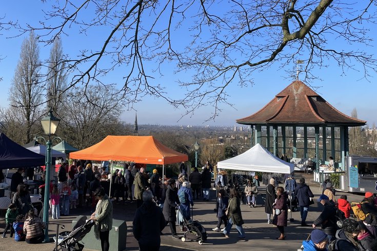 People visiting market stalls with the Horniman Bandstand in the background, with a blue sky and wintery trees above