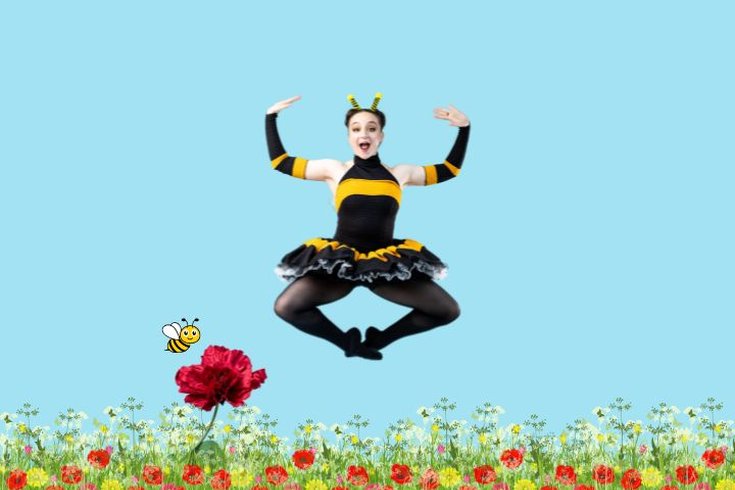 Ballet Dancer jumping in the air, dressed in a black and yellow leotard with tutu. With a garden on flowers as a backdrop